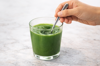 Hand stirring superfood drink with spoon in glass